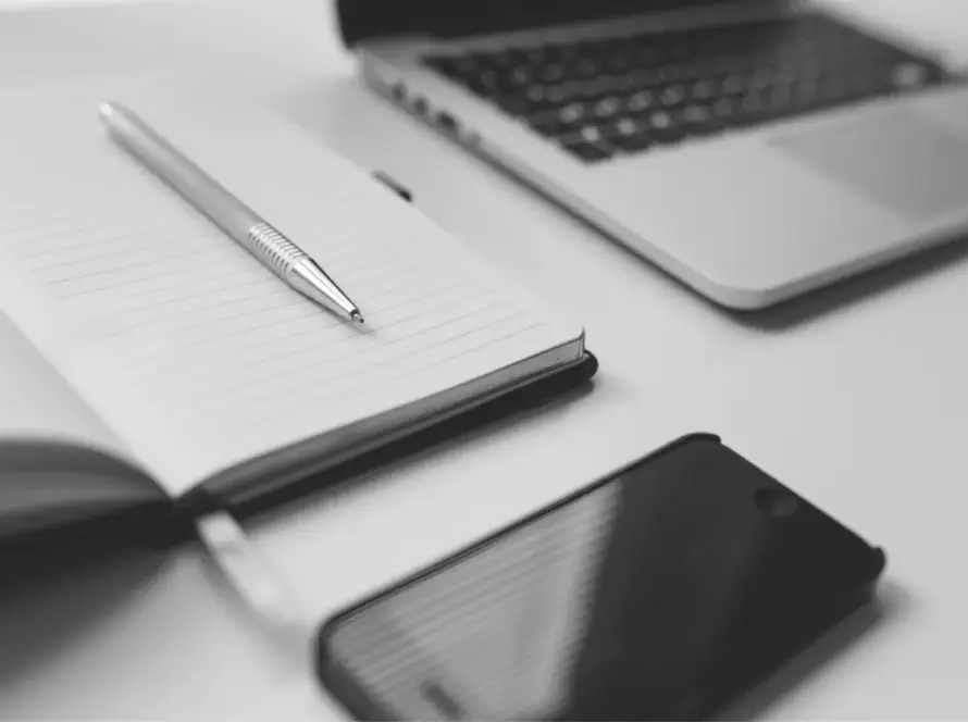 Notebook, pen, smartphone, and laptop on a desk, tools for a virtual assistant.