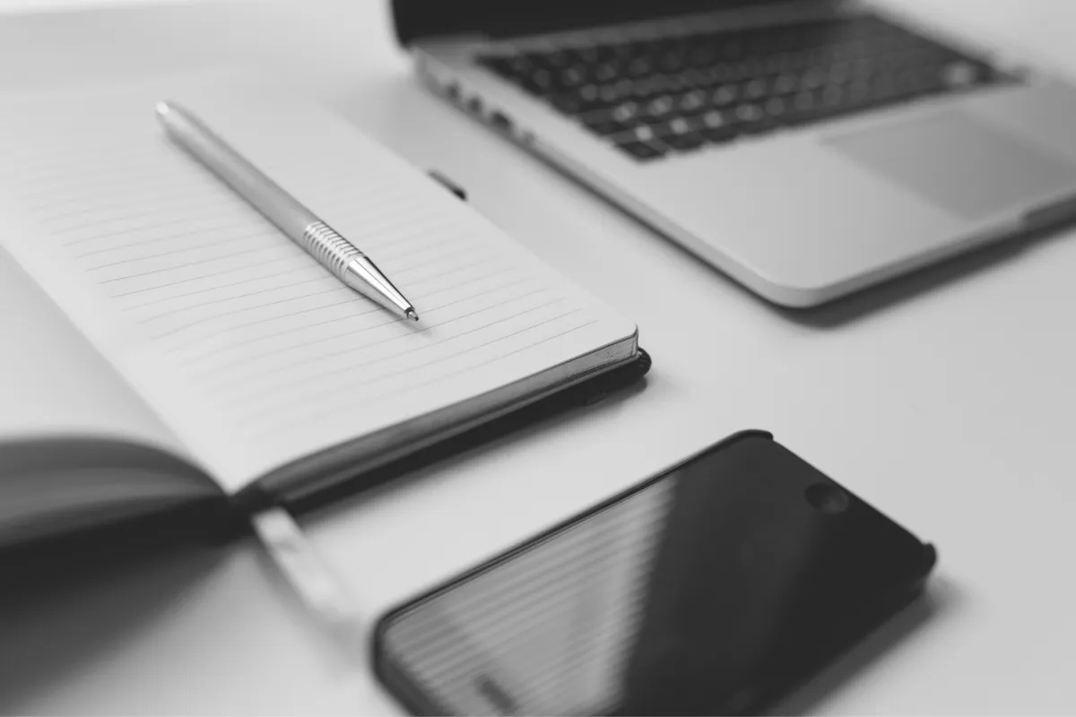 Notebook, pen, smartphone, and laptop on a desk, tools for a virtual assistant.